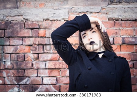 Portrait of a teenage girl with black lipstick posing next to an old brick wall. Toned effect