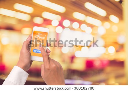Hand holding mobile with Order food online with blur restaurant background, food online business concept.Leave space for adding your text
