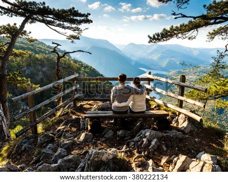 Couple sitting on a viewing platform in Serbia. Stunning views from a cliff into the river Drina Serbia through the pines. Royalty-Free Stock Photo #380222134