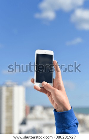 Holding mobile cell phone over city buildings business background. Closeup photo on hand with blank black screen cellphone 