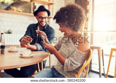 Portrait of smiling young woman at a cafe table looking at digital tablet with a friend sitting by. Royalty-Free Stock Photo #380240200