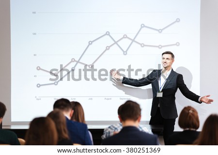 Smiling charismatic speaker giving public presentation in conference hall