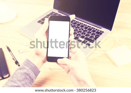 Girl with blank smartphone and opened laptop on wooden table, mock up 