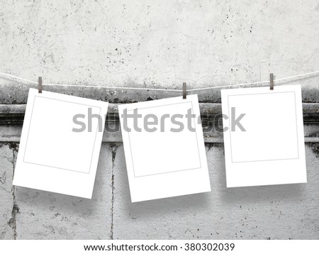 Close-up of three hanged square photo frames with pegs on gray ancient weathered wall background