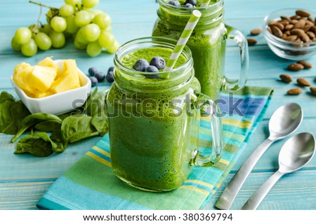 Mason jar mugs filled with green spinach and kale health smoothie with green swirled straw sitting with blue striped napkin and spoons Royalty-Free Stock Photo #380369794