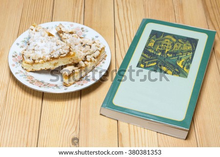 Green book with a plate of cake on a wooden board.