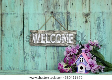 Wood welcome sign by birdhouse and purple flowers hanging on antique rustic mint green wooden background