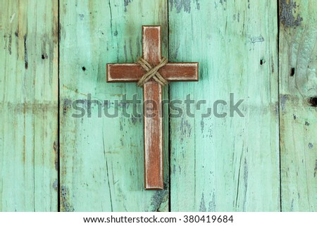 Wood cross with rope hanging on antique rustic mint green wooden background; Easter, Christmas and religious background with painted copy space