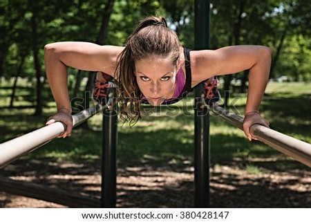 Beautiful female athlete exercising on parallel bars, doing push-ups
