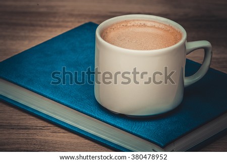 Toned photo. Color tone tuned. Cup of coffee on a wooden table with book