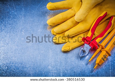 Yellow electrical tester safety gloves cutting pliers on metallic background.
