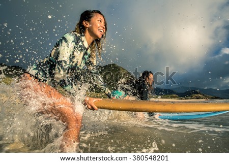 Two surfing girls on a beach smiling and ready to go into the water.
