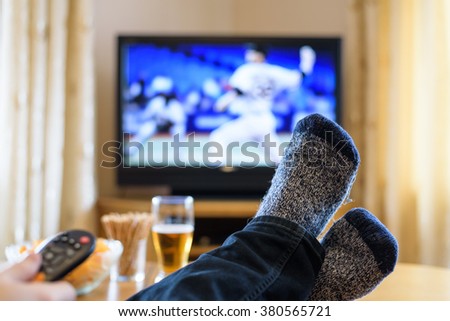 Television, TV watching (baseball match) with feet on table eating snacks and drinking beer - stock photo