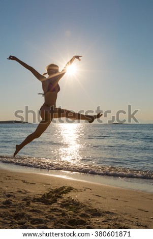 Young happy woman in swimsuit on the beach running and jumping on the seashore. Shot taken in backlit.
