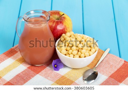Apple juice in a jug and corn balls into a bowl on a wooden background okreshennogo blue.