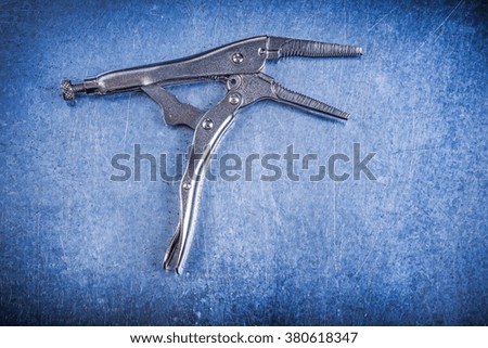 Locking pliers with open jaws on metallic background.