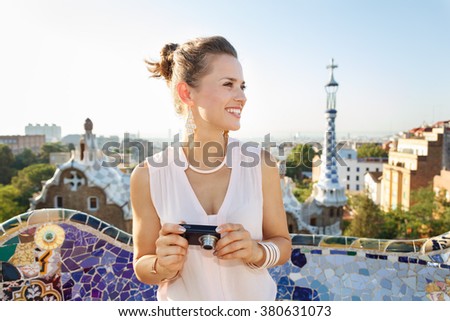 Refreshing promenade in unique Park Guell style in Barcelona, Spain. Happy young woman tourist holding digital photo camera and looking aside while in Park Guell, Barcelona, Spain
