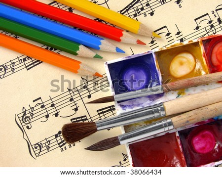 color pencils and paints with brushes on the musical notes background