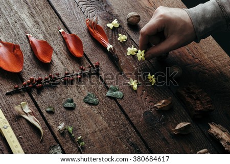 Man arranging flowers and leaves on old wooden desk