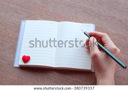hand is writing on blank notebook with red heart on wood textures

