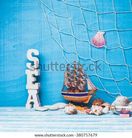 Beautiful sea composition with toy sailboat, seashell, glass bottle and fishing net on blue background