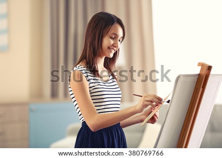 Beautiful girl painting on canvas in room