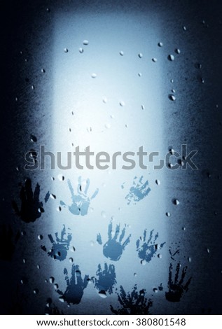 Blur background of handprints illuminated on a wet glass pane.
