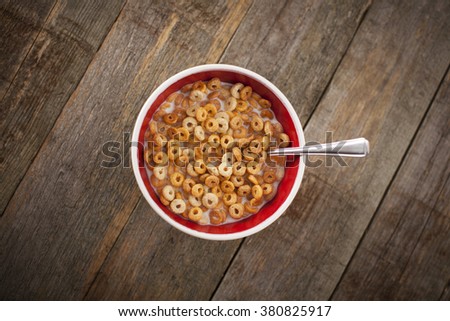 Multigrain breakfast cereal hoops in a red and white bowl covered in ice cold milk with a silver spoon. Sat on a textured wooden background/surface