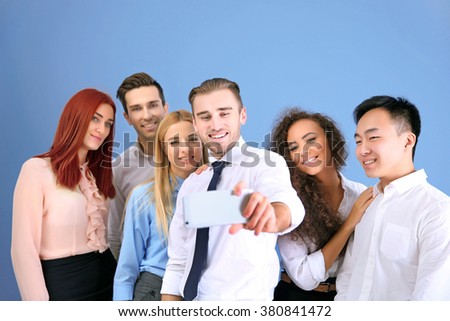 Young people making group photo with smart phone on blue wall background