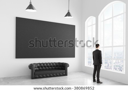 Businessman in modern white light room with chesterfield sofa and blank black poster, mock up 3D Render