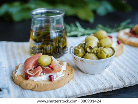 Spanish food tapas. Toasted bread with serrano ham and olives on background of olive oil with spices. Sandwiches with prosciutto. Selective focus.