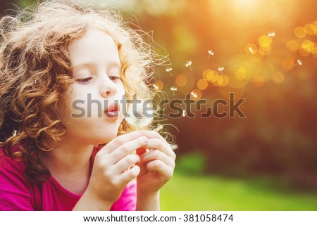 Little curly girl blowing dandelion. Royalty-Free Stock Photo #381058474