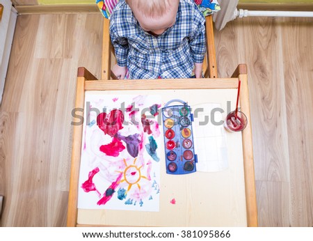 Baby boy painting with watercolors. Small caucasian child playing in home with paint and brush