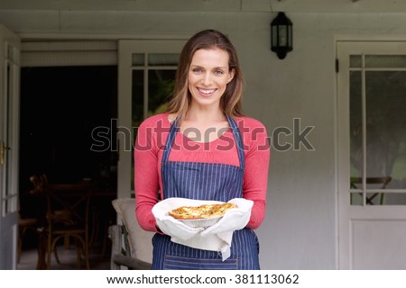 Portrait of a smiling woman holding pie in a pan Royalty-Free Stock Photo #381113062