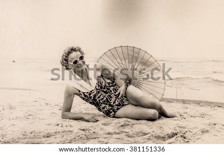 Vintage photo of woman resting on beach in swimsuit with umbrella (early 1960's) Royalty-Free Stock Photo #381151336