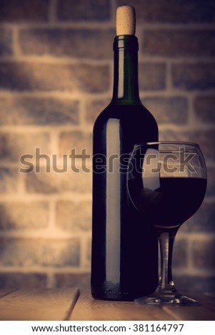 Wine bottle and glass on a wooden table with bricks wall background  toning photo