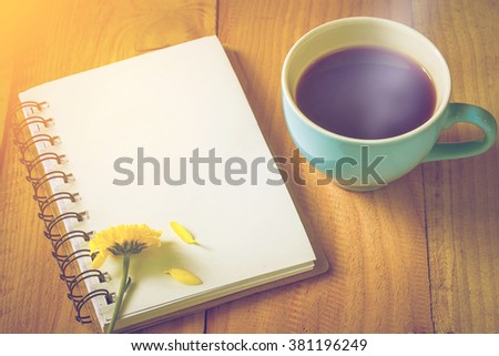 soft focus photo of notebook on wooden floor with yellow flower and blue coffee cup.vintage color tone.