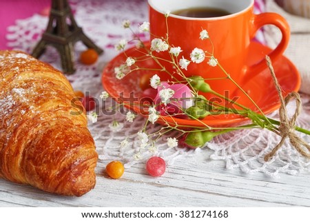 cup of coffee and croissant are decorated by the small Eiffel Tower, napkins, roses and candies on a white wooden table