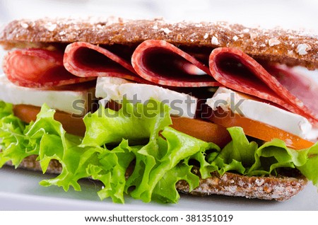 Salami and brie sandwich with whole wheat bread on white wooden background