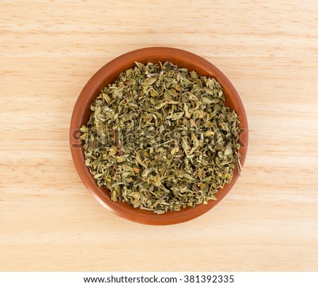 Top view of a portion of damiana leaf in a small bowl on a wood counter top.