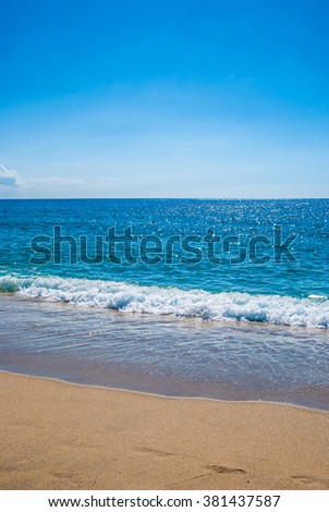 Yellow sandy beach and blue sea with waves and seafoam. Background image for travel, summer vacation, and recreation. Vivid photo of tropical paradise.