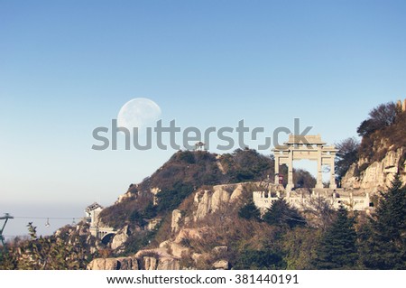 A waning moon over the mountains of Tai Shan (Mount Tai) and Peng Yuan Gate in Shandong province China in the morning light.   Royalty-Free Stock Photo #381440191