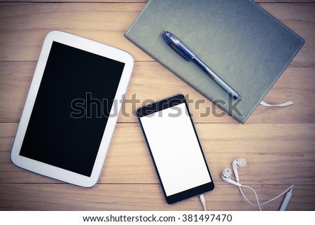 vintage image of tablet and smart phone with isolated screen and notebook paper on wooden table,business and technology concept