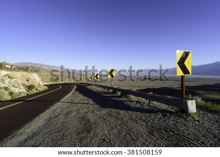 Road with traffic signs leading down into a desert valley.