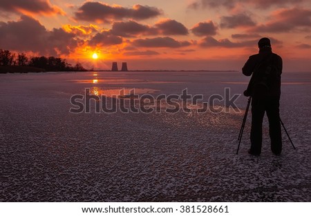 photographer takes a picture of fantastic sunset on a frozen lake