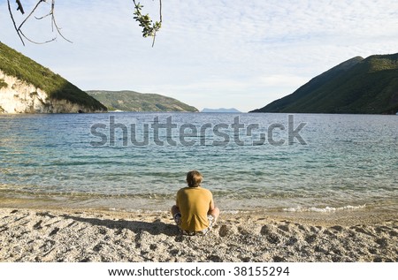 A colour landscape photo of a man sitting alone on beach.