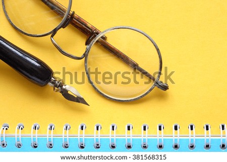 Old vintage spectacles near fountain pen on open notebook with colored pages