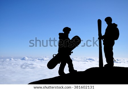 Skier and snowboarder silhouette high above the clouds in mountains. Snowboarder walking to the standing skier, colorful sky in front of them. Couple of freeriders on the hill.