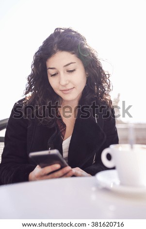 Young woman using the phone while having a coffee on a terrace