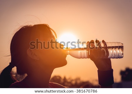 Female drinking a bottle of water silhouette.  Royalty-Free Stock Photo #381670786